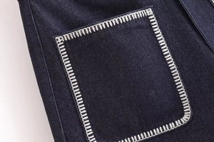 Detail of dark blue denim fabric with contrast white stitching on a large utility pocket