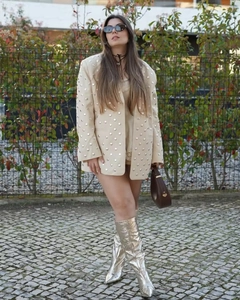 Detail eines beigen Oversize-Blazers mit Metallnieten und silbernen Metallic-Stiefeln