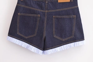 Detail view of denim shorts showing orange contrast stitching and white pleated hem