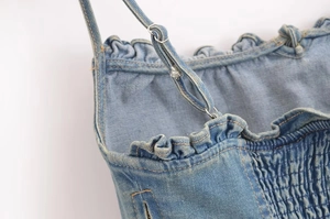 Dettaglio del top in denim lavato con tessuto elasticizzato a punto smock e volant