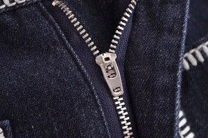 Close-up of metal zipper closure and white stitching on dark blue denim jeans