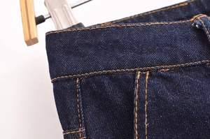 Detailed macro view of dark blue denim waistline with classic orange contrast stitching