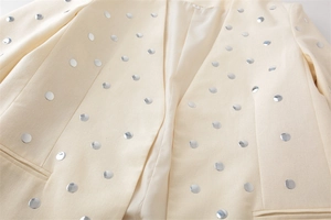 Nahaufnahme von silbernen Metallnieten auf cremefarbenem Blazer und Kragendetails