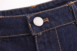 Detailed macro view of denim waistband with orange stitching and silver metal button