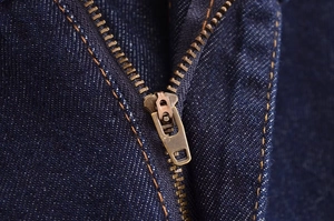 Detailed close-up of dark blue denim shorts featuring a bronze zipper and orange stitching