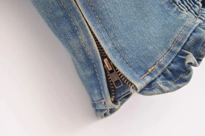 Dettaglio ravvicinato di una cerniera in metallo e bordi a balze su denim lavato