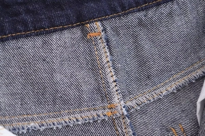 Macro shot of dark blue denim stitching showing reinforced orange seams and twill texture