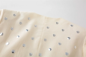Detailansicht der silbernen Pailletten und Nieten auf dem cremefarbenen Blazer