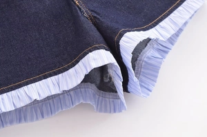 Detailed close-up of dark denim shorts featuring blue striped ruffle hem and contrast stitching