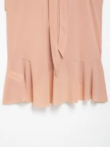 Detailed macro view of the ruffled hem and tie waist on this light pink crepe fabric top