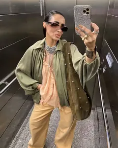Mirror selfie showing olive green pilot jacket with ruffled blouse and retro jewelry set