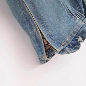Dettaglio macro di top in denim lavato con cuciture arancioni e cerniera in metallo