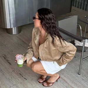 Women's light brown suede lapel jacket styled with white skirt and brown open-toe heels