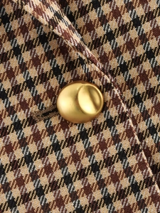 Dettaglio di un blazer pied-de-poule con un grande bottone in metallo dorato opaco