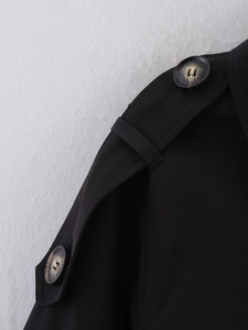 Detail of black trench coat shoulder featuring buttoned epaulet with tortoiseshell texture
