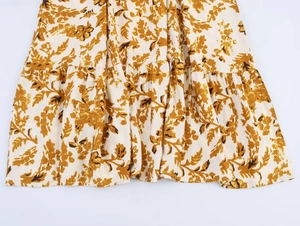 Detail view of tiered ruffle hem on a cream dress with mustard leaf print patterns