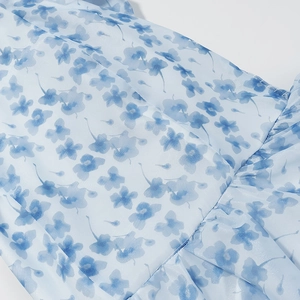 Close-up of blue floral chiffon fabric showing fine stitching and pleated ruffle detail