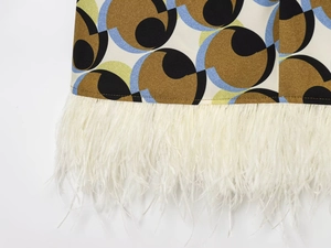 Close-up of geometric circle print fabric with elegant white feather trim on the hemline