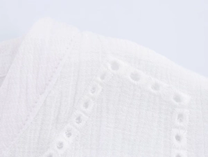 Macro detail of white crepe fabric with elegant eyelet embroidery and diamond patterns