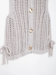 Detail of chunky hollow-knit vest featuring golden buttons and side bow-tie accents