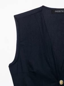 Detail of dark blue linen vest featuring a V-neckline and gold cylindrical button