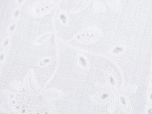 Close-up of white cotton fabric featuring intricate floral embroidery and eyelet details