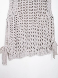 Detailed close-up of light gray chunky knit sweater featuring side bow tie decorations