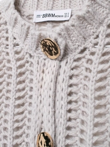 Detail of grey chunky knit sweater featuring hollow weave texture and a gold metal button