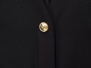 Close-up of a gold hammered metal button on a black crepe midi dress with texture detail