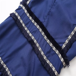 Détail d'une robe bleu foncé avec bordure à franges de style ethnique et ruban noir et blanc