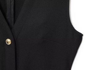 Detail of V-neckline featuring a hidden zipper and polished gold metal button on black fabric