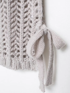 Close-up of chunky knit pattern with cable stitch and bow detail on light grey sweater