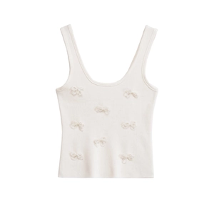 Detail of white knit camisole featuring delicate 3D bow embellishments and soft texture