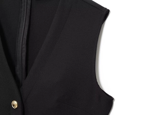 Detail of V-neckline on black vest dress featuring an ornate gold button and zipper