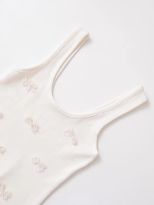 Close-up of cream knit tank top with delicate pearl bow accents and ribbed texture