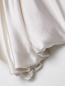 Close-up of cream satin fabric showing elegant draped pleats and silky texture