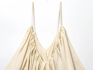 Detailed macro view of cream satin fabric with pleated v-neckline and spaghetti straps