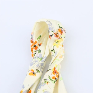 Gros plan sur un bandeau floral jaune en tissu avec détail torsadé et motifs de fleurs vives