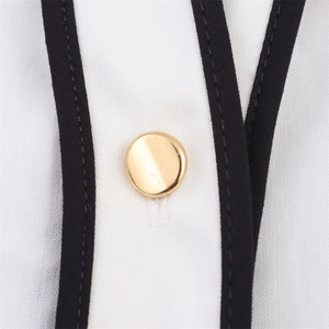 Close-up of golden metal button on white shirt fabric with black contrast piping detail