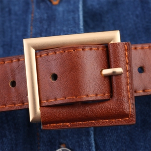Macro detail of brown leather belt with gold buckle on denim fabric background