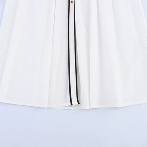 Close-up of white dress hem featuring black contrast trim and a metallic gold button detail