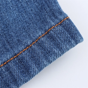 Detailed close-up of dark blue denim fabric with contrast orange stitching on the seam