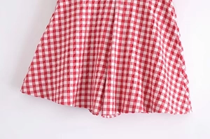 Close-up detail of red and white gingham fabric with pleated texture on casual shorts