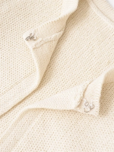 Détail macro du cardigan en maille crème avec fermetures à agrafes métalliques argentées
