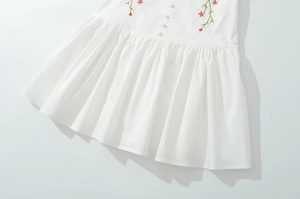 Detail of white cotton dress hem with floral embroidery and fabric buttons