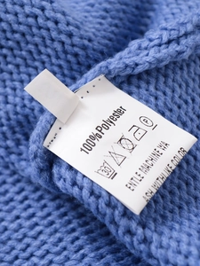 Close-up of blue knit sweater texture and white care label showing 100% polyester fabric