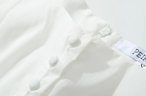 Macro shot of white sleeveless dress with fabric buttons, invisible zipper and size label
