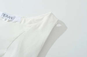 Detailed macro shot of the PEIRAN brand label and size S tag on white sleeveless dress