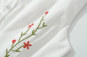 Close-up of vibrant floral embroidery and fabric buttons on white sleeveless dress