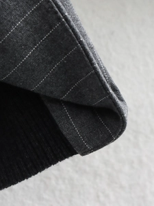 Macro detail of dark grey pinstripe fabric and black ribbed knit cuff of the jacket